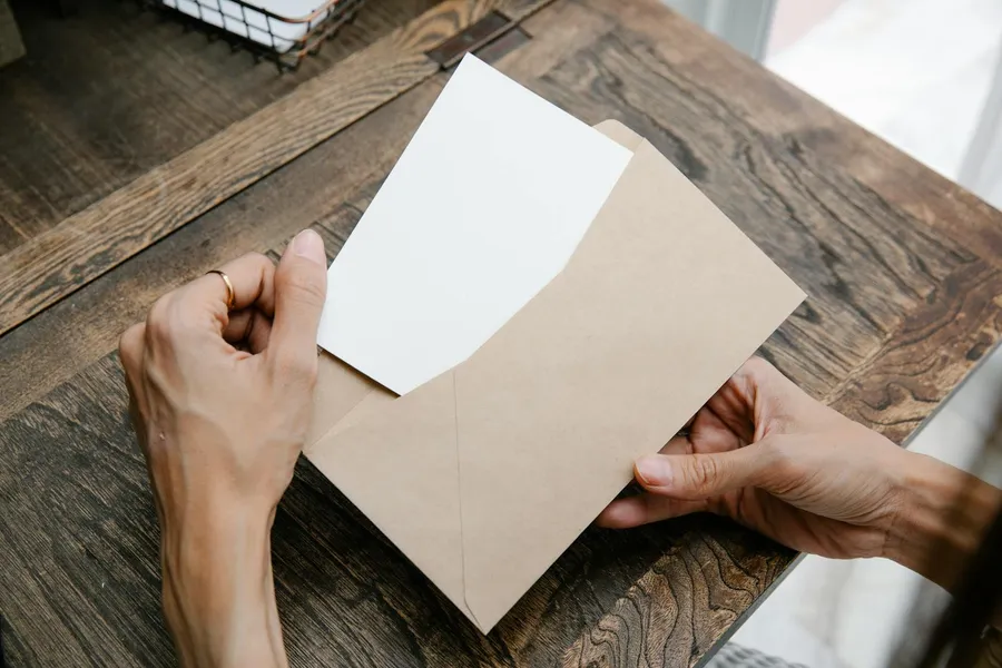 Mains tenant une enveloppe ouverte sur une table en bois, courrier de demande de résiliation d'assurance auto