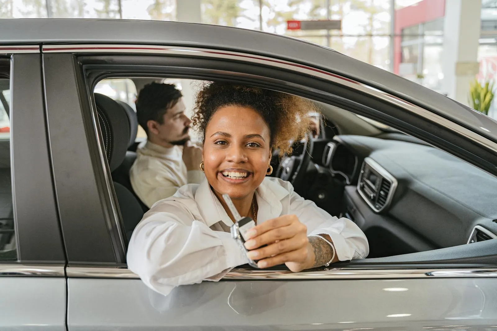 Conductrice souriante montrant les clés de sa nouvelle voiture à la fenêtre du véhicule