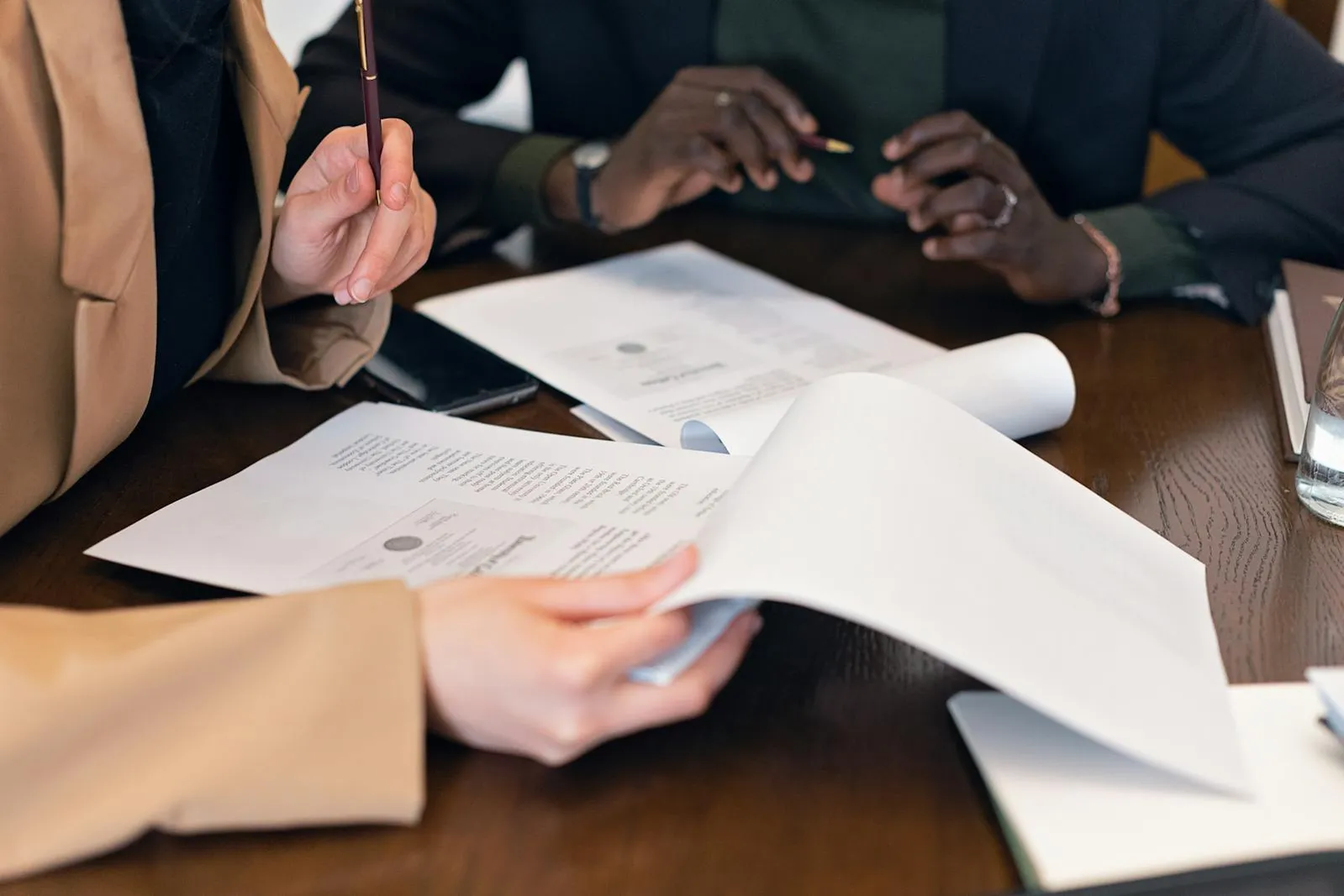 Deux personnes en costume revoyant ensemble plusieurs documents avec stylos sur un bureau en bois
