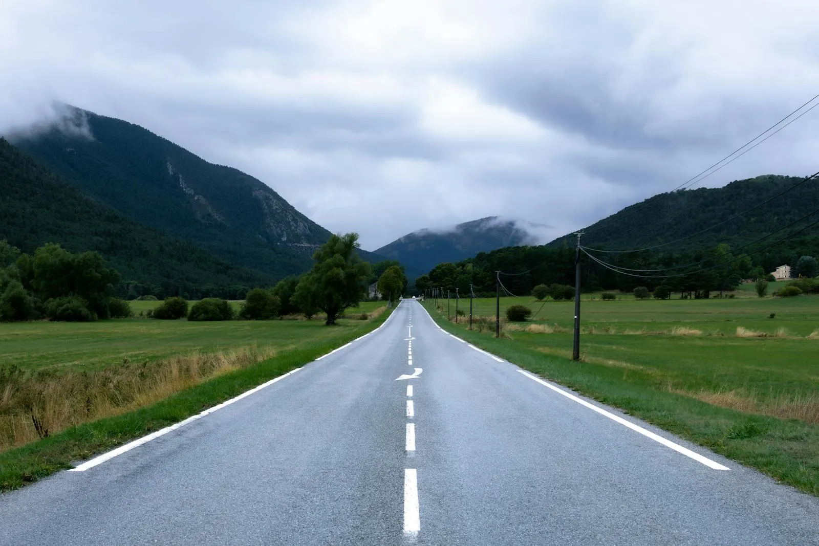 Route nationale française avec marquage au sol caractéristique traversant un paysage de montagnes sous ciel nuageux