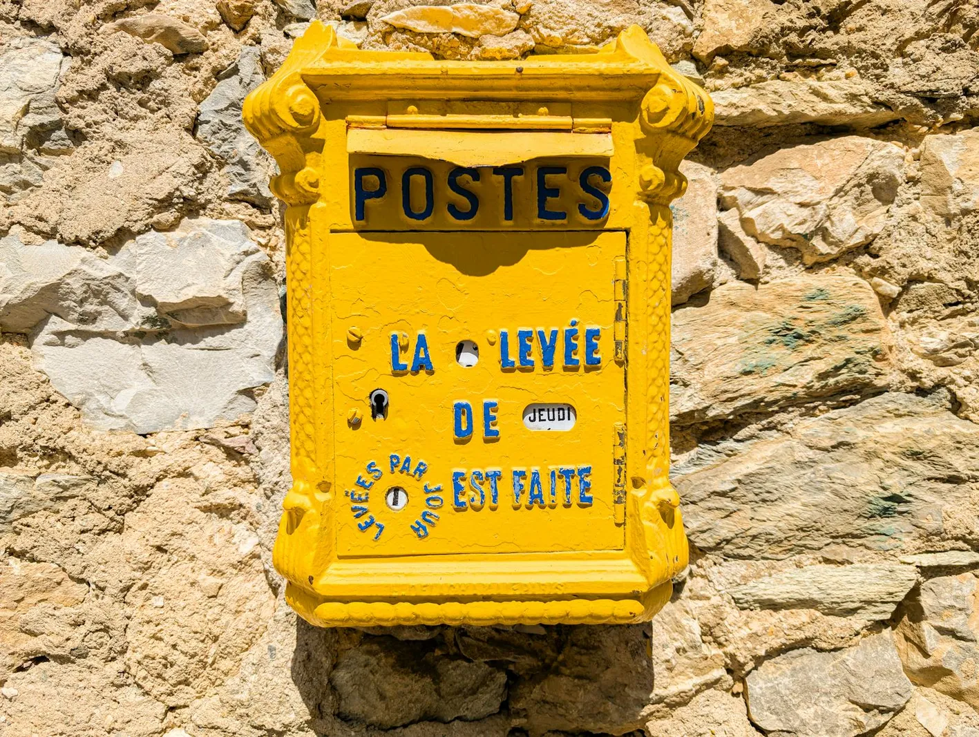 Ancienne boîte aux lettres POSTES jaune fixée sur un mur en pierre en plein jour