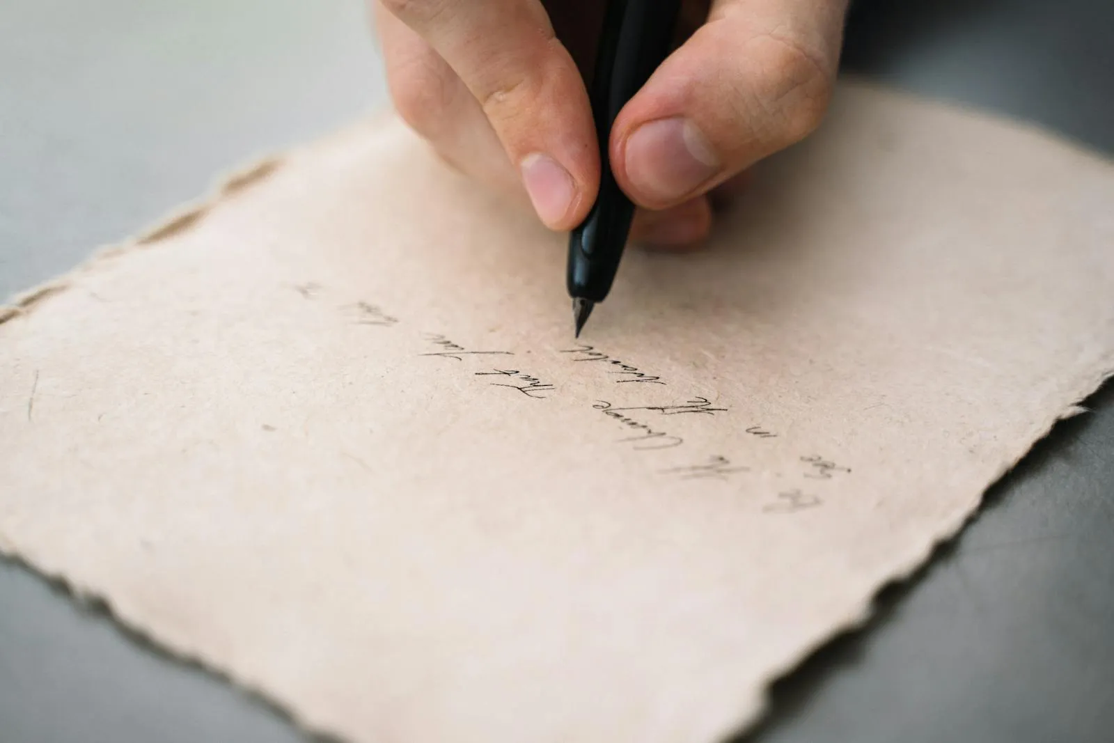 Main écrivant à la plume sur un papier texturé aux bords irréguliers posé sur une table claire