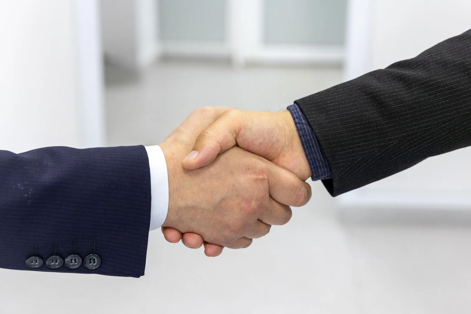 Poignée de main entre deux personnes en costume foncé devant un fond clair de bureau