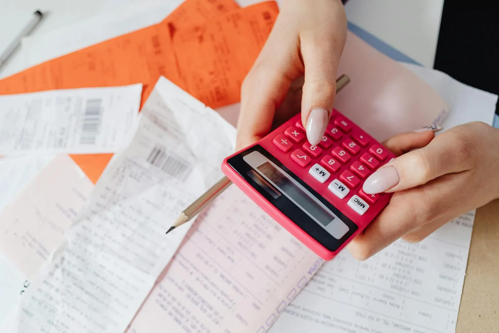Mains tenant une calculatrice rose au-dessus de reçus et de factures posés sur un bureau de travail